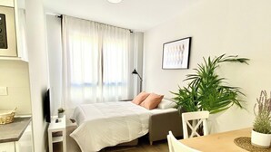 A modern, well-lit bedroom with a bed, bedside table, and a small table with chairs. - Vivodomo | New, super location, optional parking (Madrid)