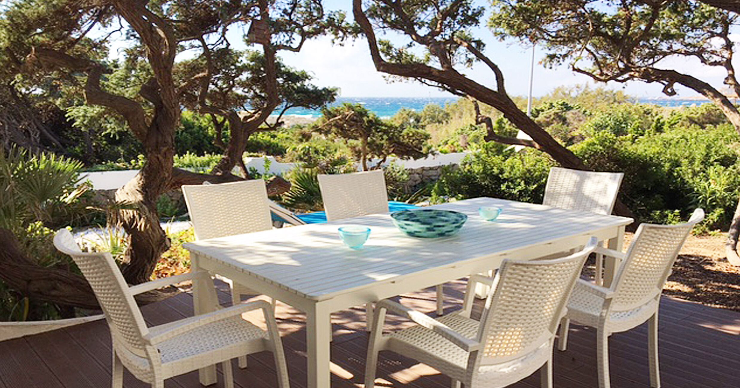 A white table and chairs set on a deck with a view of the ocean and trees.