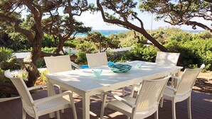Un conjunto de mesa y sillas blancas en una terraza con vista al océano y a los árboles.