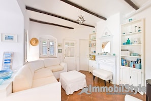 A spacious living room with a white sofa, a matching ottoman, and a bookshelf filled with books and decorative items.