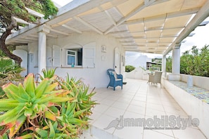 A covered outdoor area with a white pergola, a blue chair, and a tiled floor.