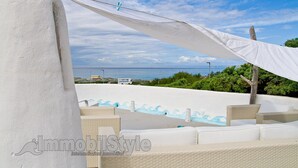 Una terraza en la azotea con toldo blanco, mobiliario de mimbre y vista al mar.