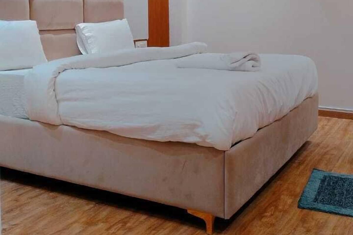A modern bedroom with a large bed, wooden headboard, and an air conditioning unit on the wall.