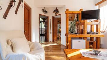 Una habitación acogedora con piso de madera, un sofá, un televisor sobre un mueble de madera y una mesita con un bol.