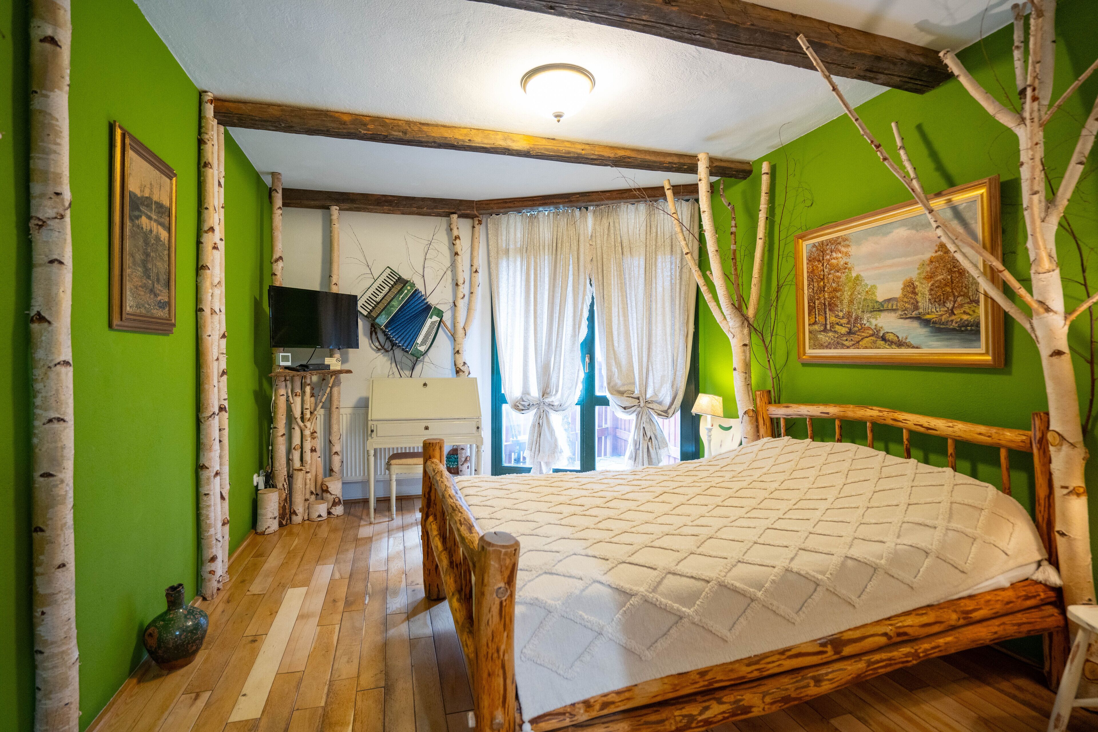 Quarto com cama de madeira, paredes verdes, televisão e janela com cortinas.