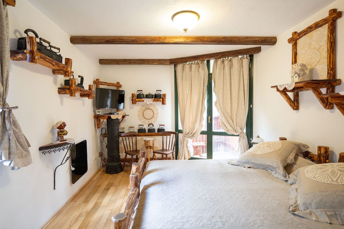 A cozy room with a bed, wooden beams, a television, and a small table with chairs.