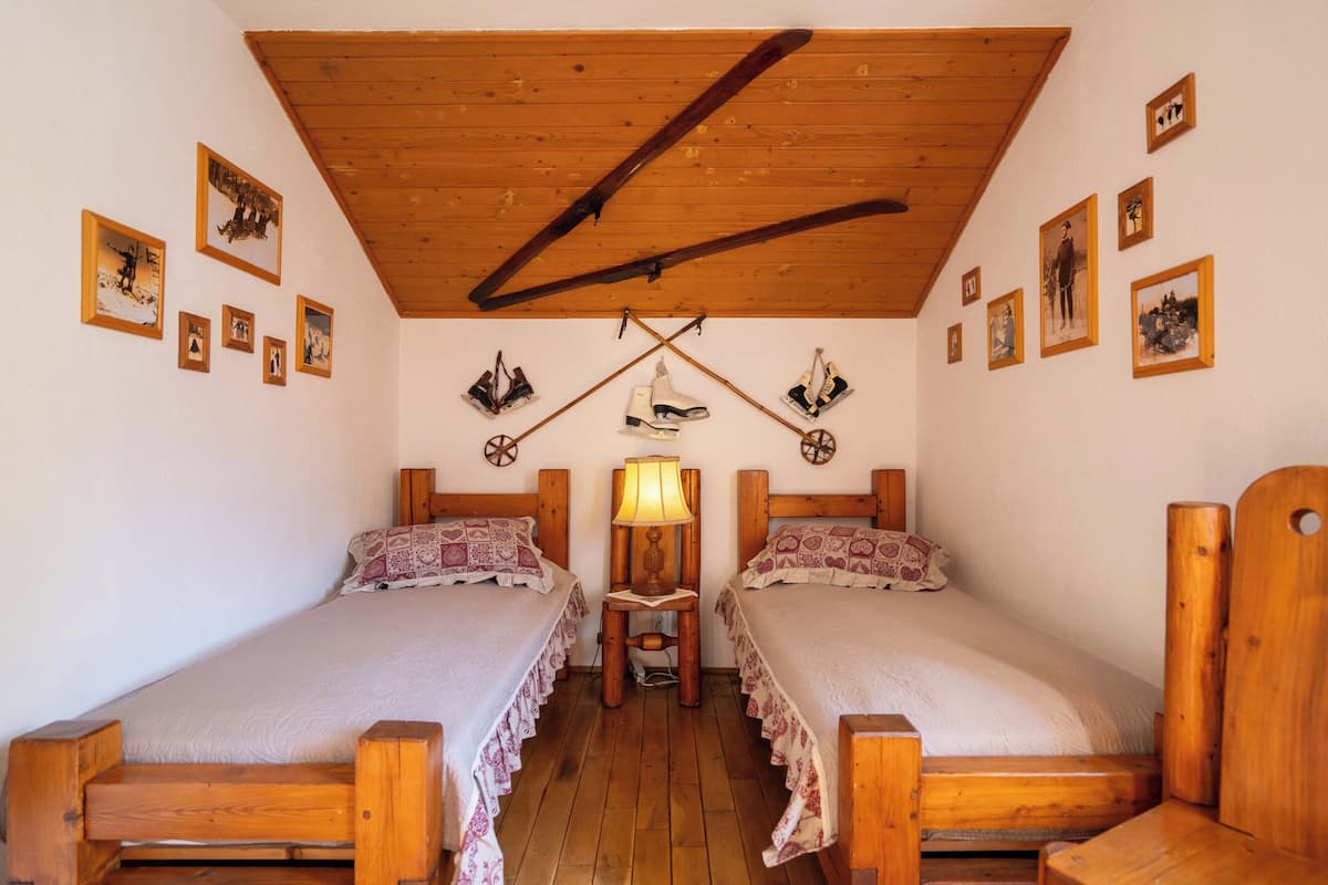 A room with two wooden beds, a wooden ceiling, and several framed pictures on the walls.