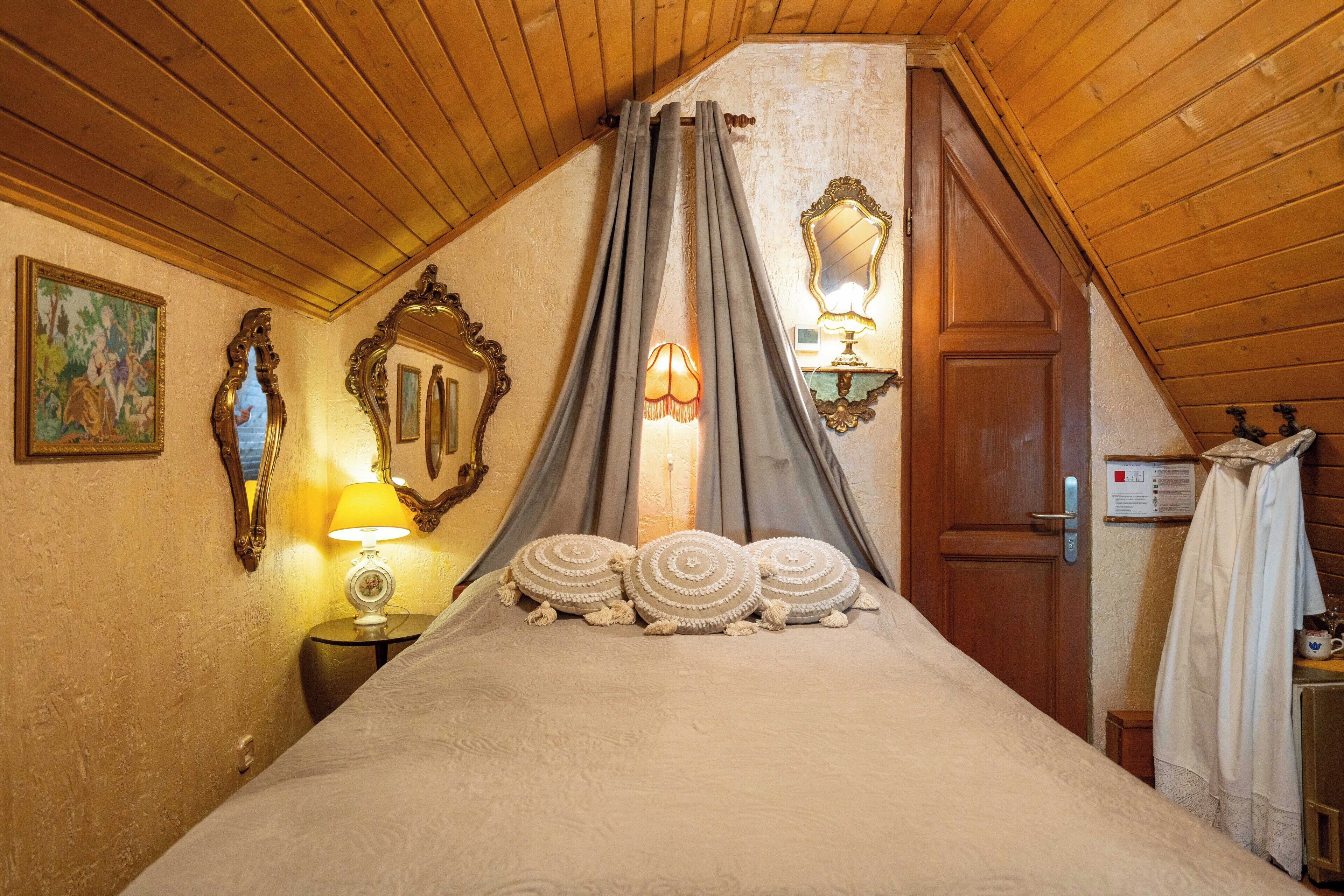 Un dormitorio con techo de madera, cama con ropa de cama blanca, mesita de noche con lámpara y un espejo en la pared.