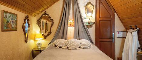 Un dormitorio con techo de madera, cama con ropa de cama blanca, mesita de noche con lámpara y un espejo en la pared.