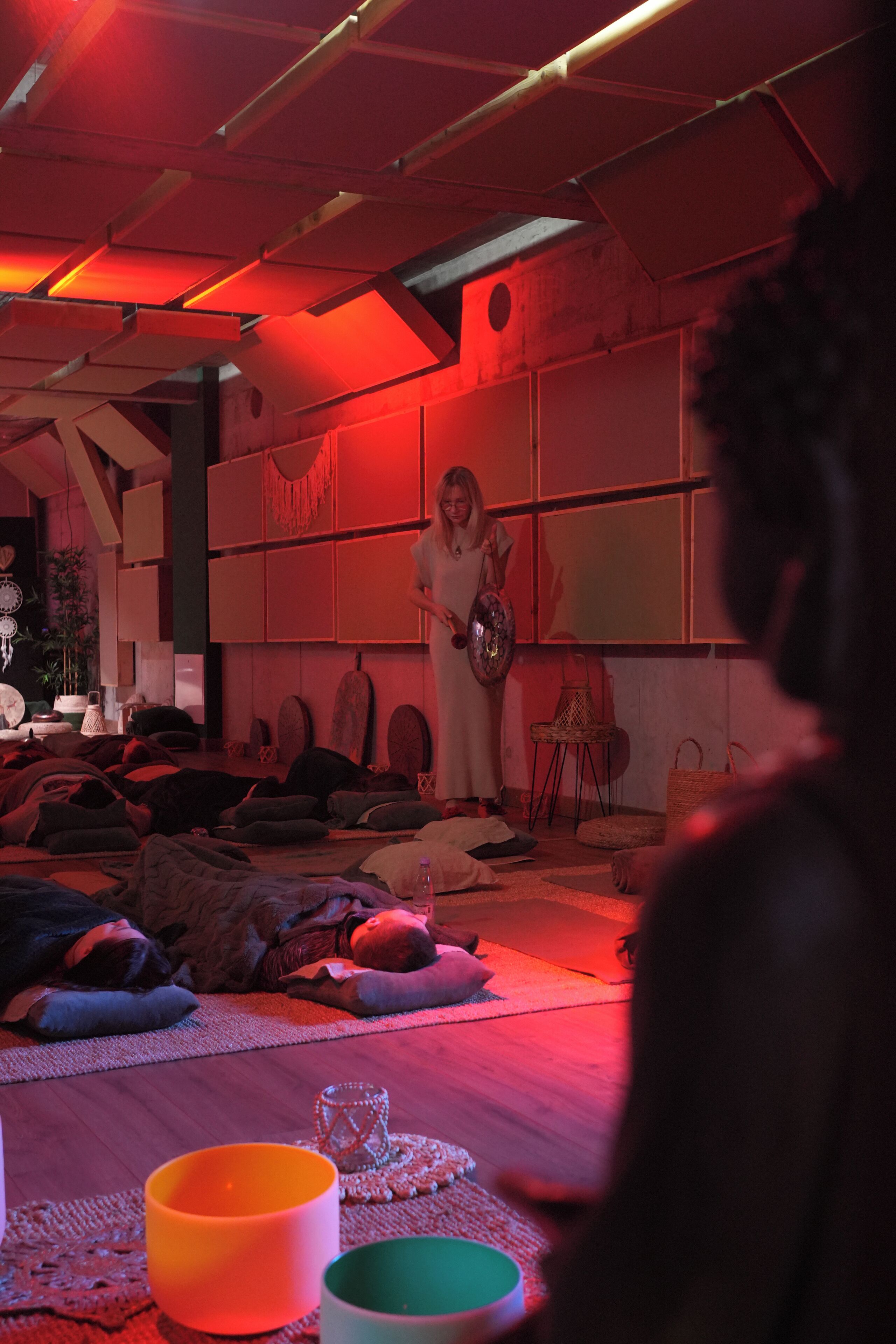 A room with a low ceiling, exposed beams, and a red ambient light. There are several cushions and a small table with a glass object on it.