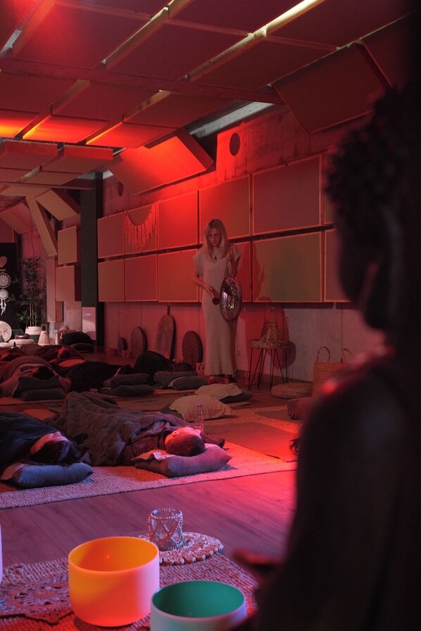 A room with a low ceiling, exposed beams, and a red ambient light. There are several cushions and a small table with a glass object on it.