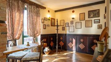 Quarto com piso de madeira, uma mesa com cadeiras, um vaso e um candelabro.
