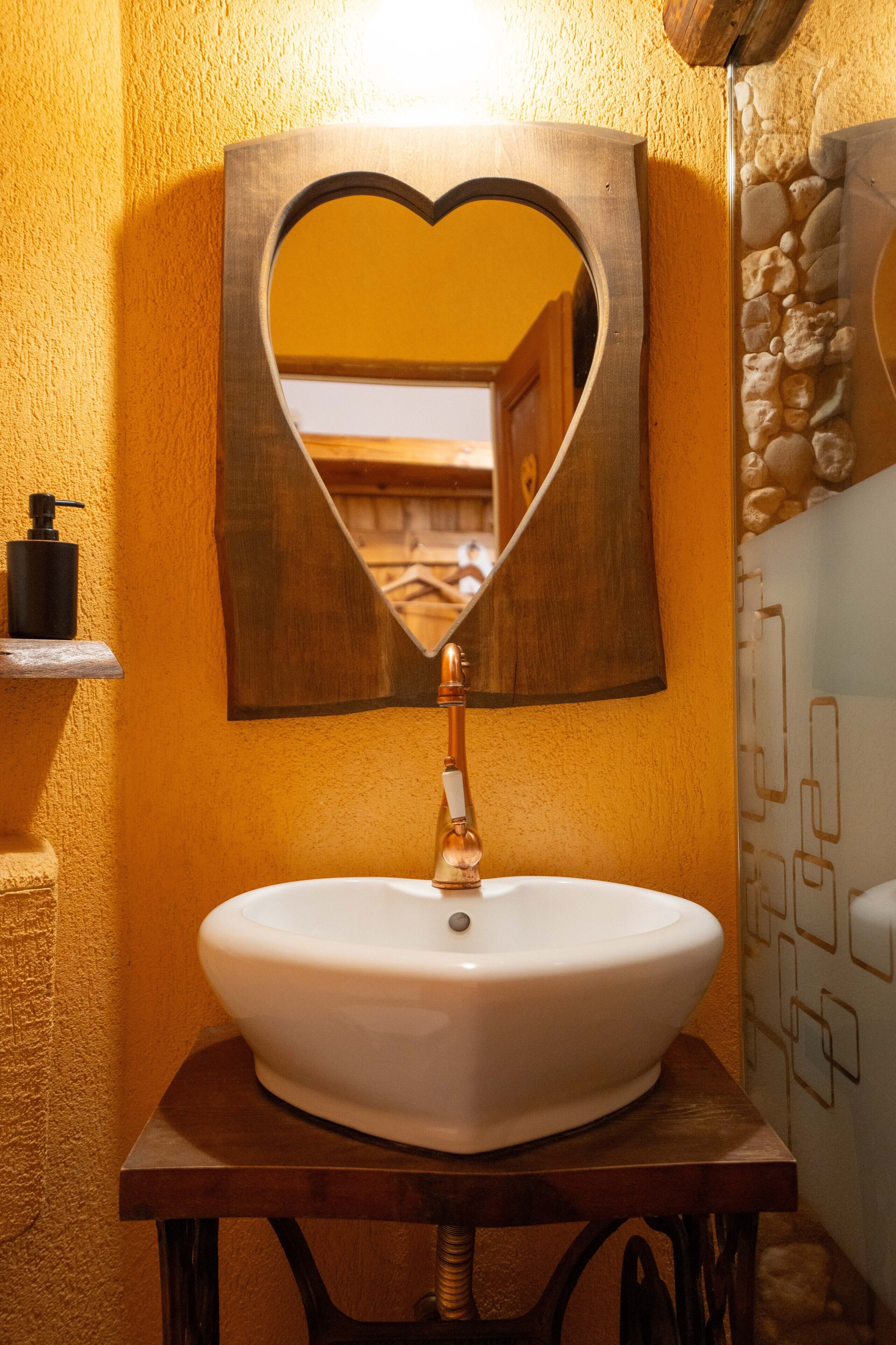 A bathroom with a white sink, a heart-shaped mirror, and a stone wall.