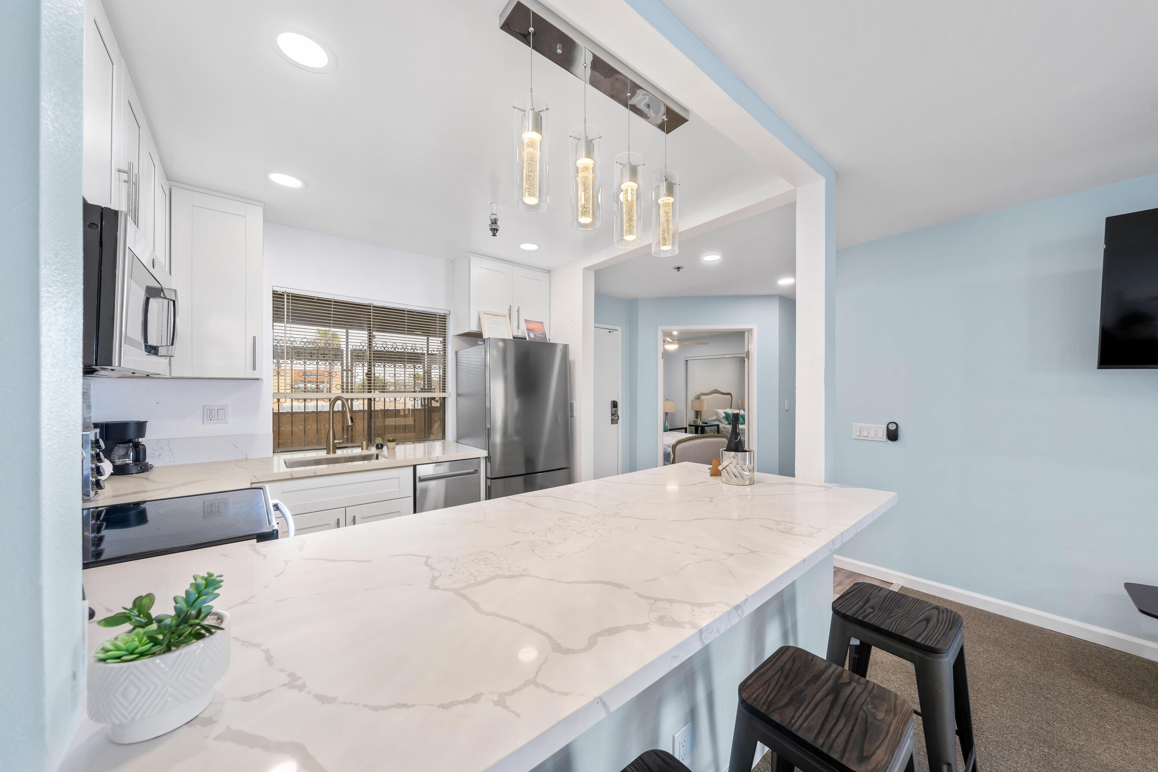 Une cuisine moderne dotée d’un grand îlot central, d’appareils électroménagers en acier inoxydable et de luminaires suspendus.