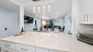 Een moderne keuken met een groot marmeren eiland, witte keukenkastjes en hanglampen.
