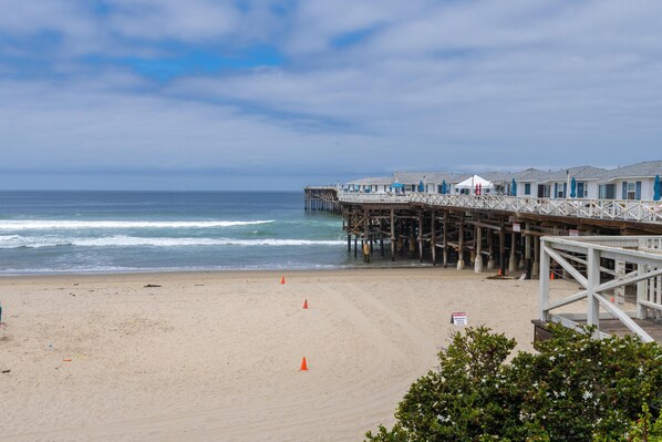 A beach with a wooden pier extending into the ocean, featuring several beachside cabins. - Remodeled beach front condo with ocean views (San Diego)