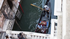 En smal kanal med en gondol, passagerare och en person som står på en bro.