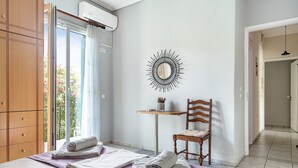 Une pièce comprenant un lit, une chaise, une petite table, un miroir et une fenêtre donnant sur l’extérieur.