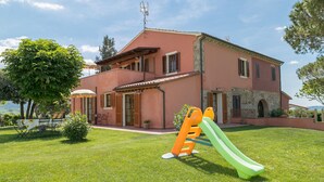 Ein zweistöckiges Haus mit roter Fassade, einem grünen Rasen und einer Rutsche für Kinder.