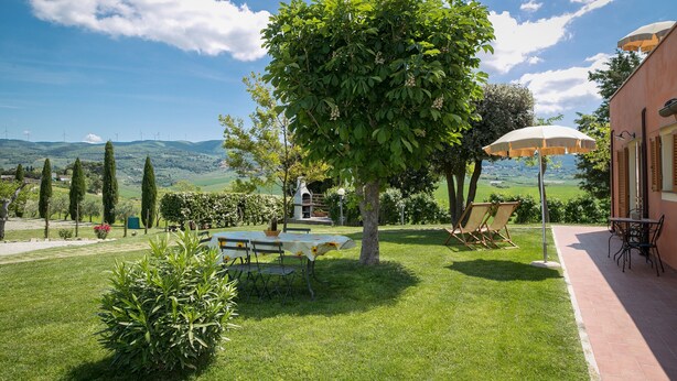 Ein Garten mit Tisch und Stühlen, ein Baum und ein Gebäude mit Blick auf die Hügel.
