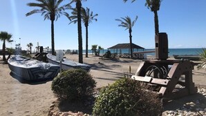 Una playa con palmeras, un área de descanso techada y un bote.