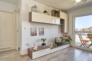 Una sala de estar moderna con televisor, estantes de madera, objetos decorativos y vistas a través de un ventanal.
