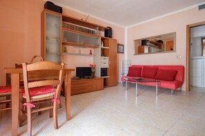 A living room with a wooden dining table, chairs, a red sofa, a TV, and a bookshelf.