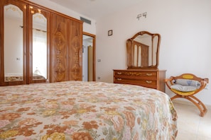 A bedroom with a floral bedspread, wooden wardrobe, and a mirror.