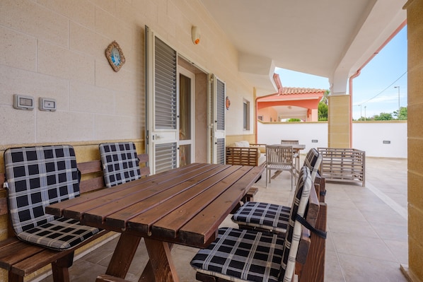 An outdoor patio with a wooden table and benches, a covered area with a red roof, and a wall-mounted security camera.