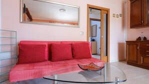 Una stanza con un tavolino da caffè in vetro, un divano rosso, un mobiletto in legno e uno specchio appeso al muro.