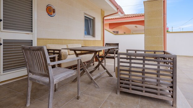 Una terrazza con tavolo e sedie, una panca di legno e un piatto decorativo appeso al muro.