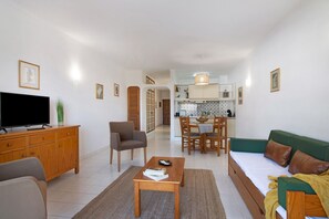 Un salon comprenant un téléviseur, un canapé, une table basse et un coin repas avec des chaises et une table.