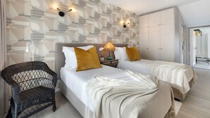 Une chambre avec deux lits, une chaise en osier, un luminaire fixé au mur et une armoire.
