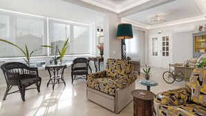 Un hall d’entrée spacieux avec une grande fenêtre, un fauteuil à motifs, des chaises en osier, une petite table avec une lampe et un vélo.