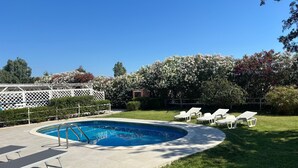 Piscina cercada por um deck, cadeiras de descanso e um jardim murado.