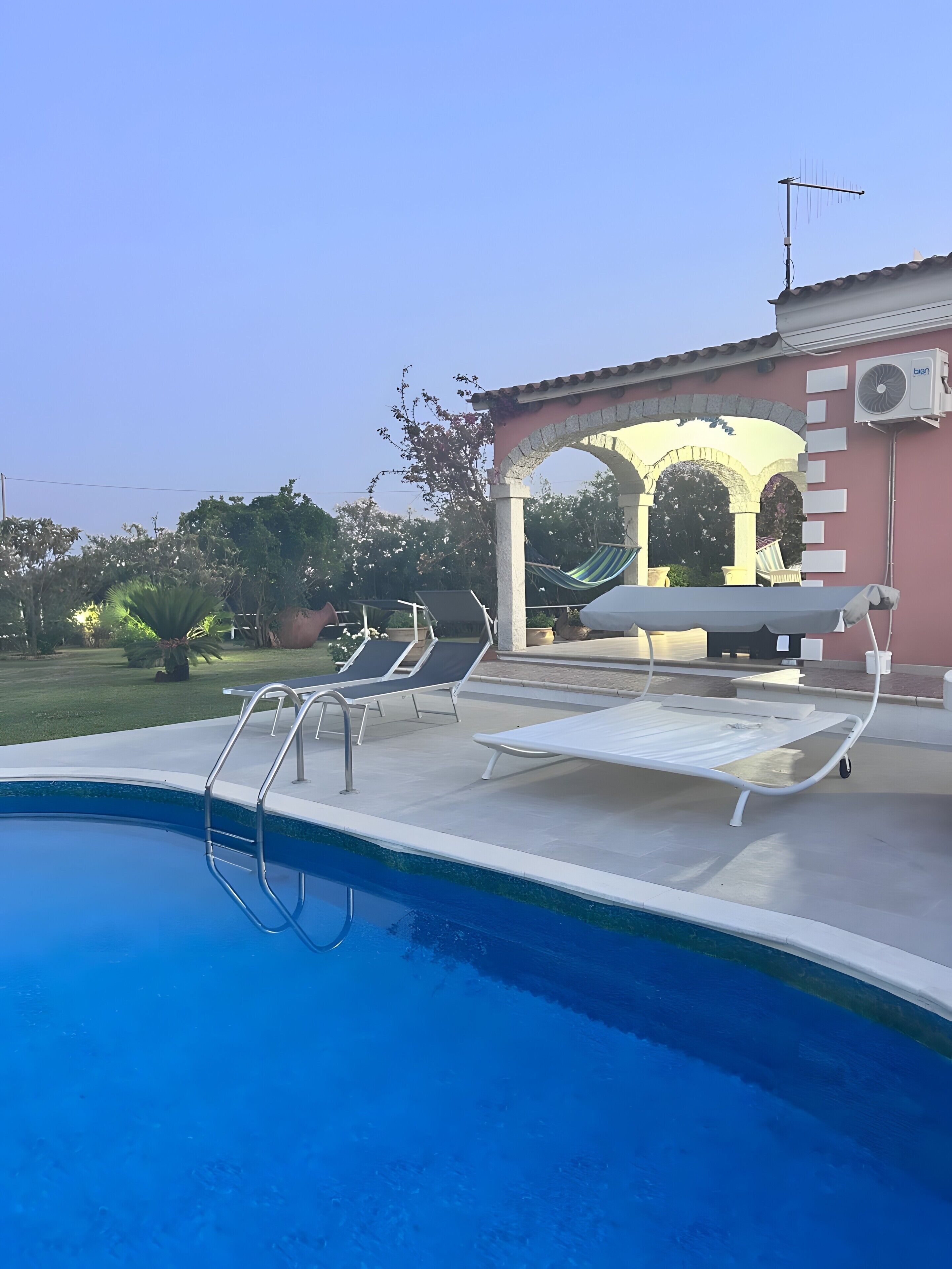 Una piscina con lettini, una pergola e un edificio con condizionatore.
