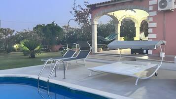 Una piscina con lettini, una pergola e un edificio con condizionatore.