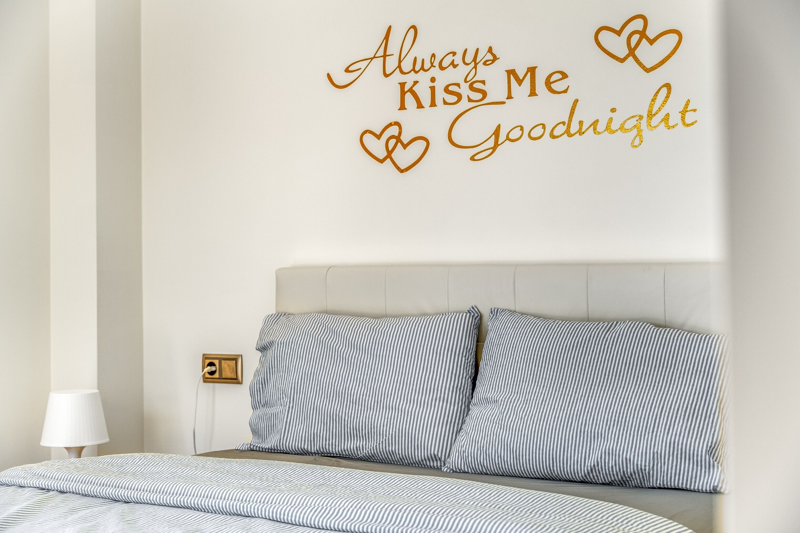 Un dormitorio con ropa de cama a rayas, cabecera y vinilo decorativo con corazones y texto.