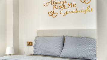 Un dormitorio con ropa de cama a rayas, cabecera y vinilo decorativo con corazones y texto.