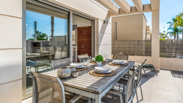 An outdoor dining area with a wooden table, chairs, and a glass enclosure. - Villa "Casa Imjo Groundfloor" with Private Pool, Private Terraces & Air Conditioning (Orihuela Costa)