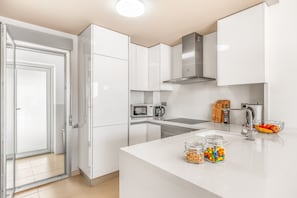 Una cocina moderna con armarios blancos, una campana extractora de acero inoxidable, un microondas y un hervidor.