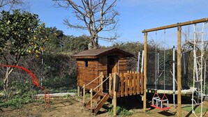 Una casita de juegos de madera con rampa y un columpio en un patio cercado.