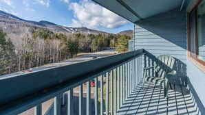 A balcony with a view of a road and trees, a chair, and a window. - Brookside II B-304 - Sunday River Slopeside Condominium (Newry)