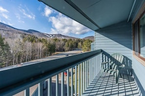 Un balcón con vista a una carretera y árboles, una silla y una ventana.