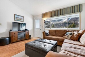 Un salón con televisor, sofá, reposapiés y ventana con vista a un pueblo.
