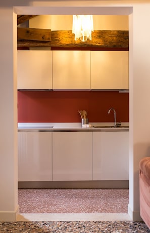 Une cuisine de taille réduite avec des meubles blancs, un pare-feu rouge et un plan de travail en granit.