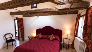 Une chambre à coucher avec un grand lit, des poutres en bois, une chaise, deux tables de chevet et une fenêtre avec des rideaux.