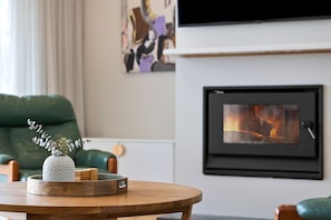 A living room with a fireplace, a green sofa, a wooden coffee table with a decorative vase, and a framed picture above the fireplace.