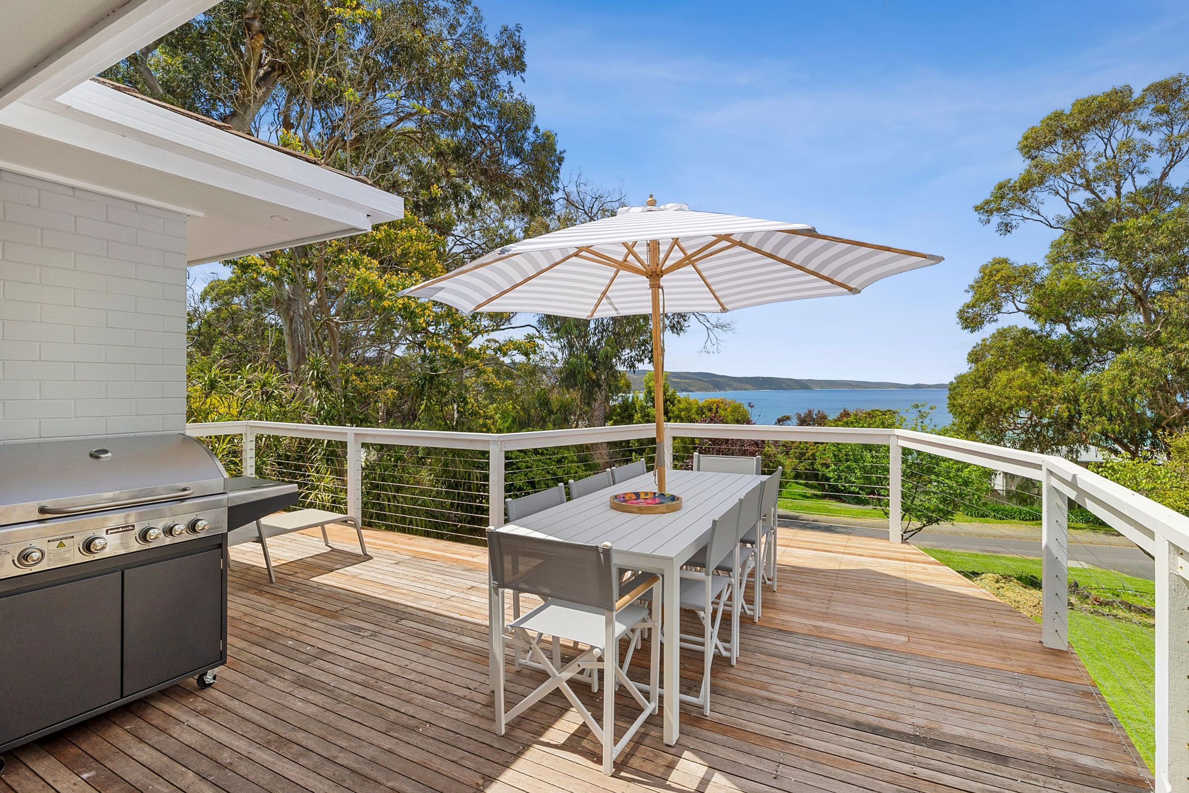 A deck with a barbecue grill, a table with chairs, and an umbrella.