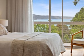 A bedroom with a large bed, a chair, a window with a view of a lake and hills. - Alby's - Beachfront Retreat (Lorne)